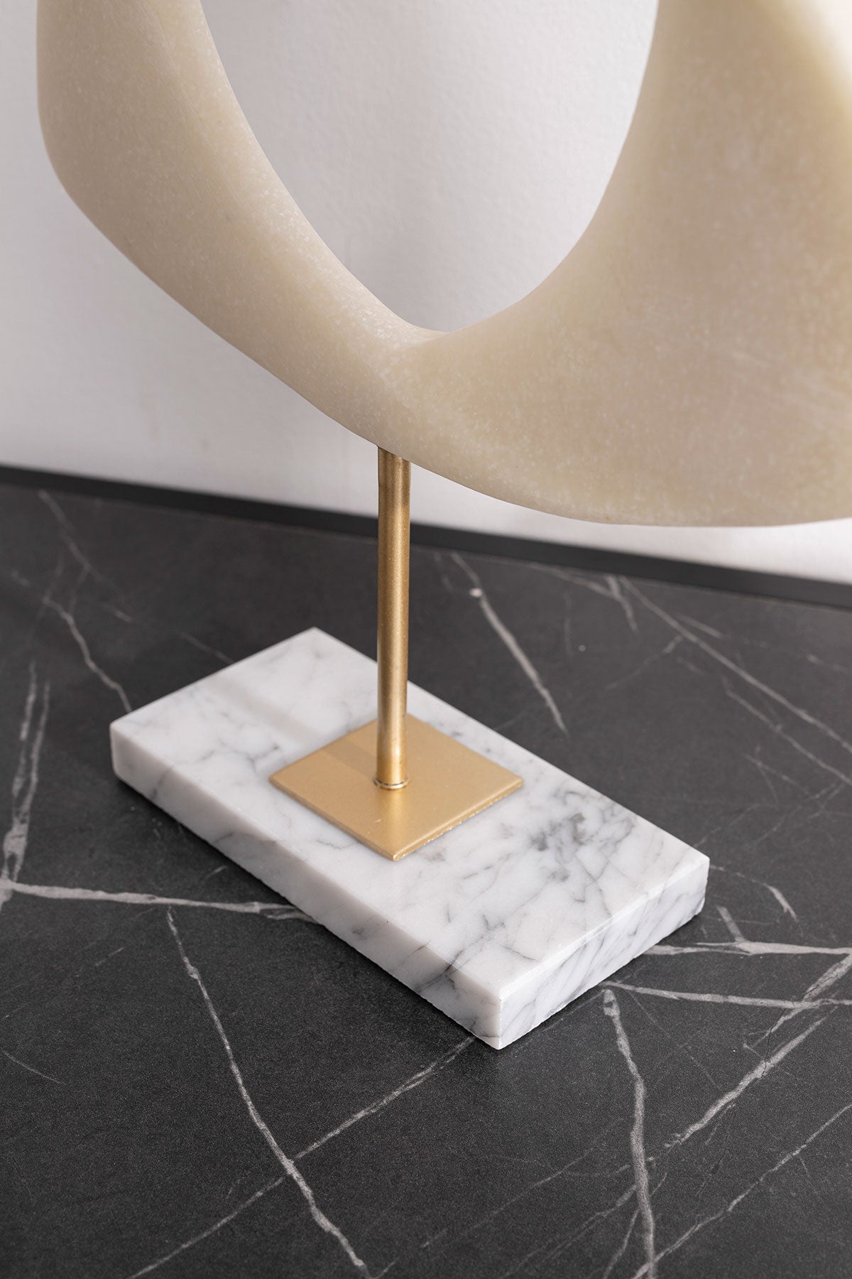 Escultura abstracta Cyclades en piedra blanco roto y soporte dorado sobre mármol veteado. Ideal para decoración minimalista o contemporánea.
