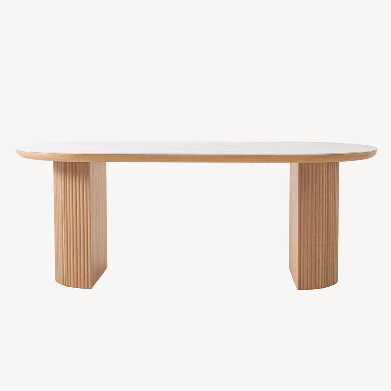 Mesa fija Colosseum con sobre ovalado porcelánico efecto mármol y base acanalada de madera de nogal. Diseño escultural para comedor moderno.